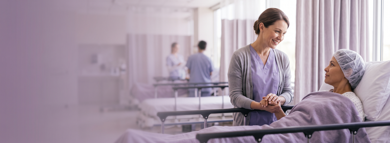 Nurse in lavender scrubs smiles and holds hands with a patient in a hospital bed